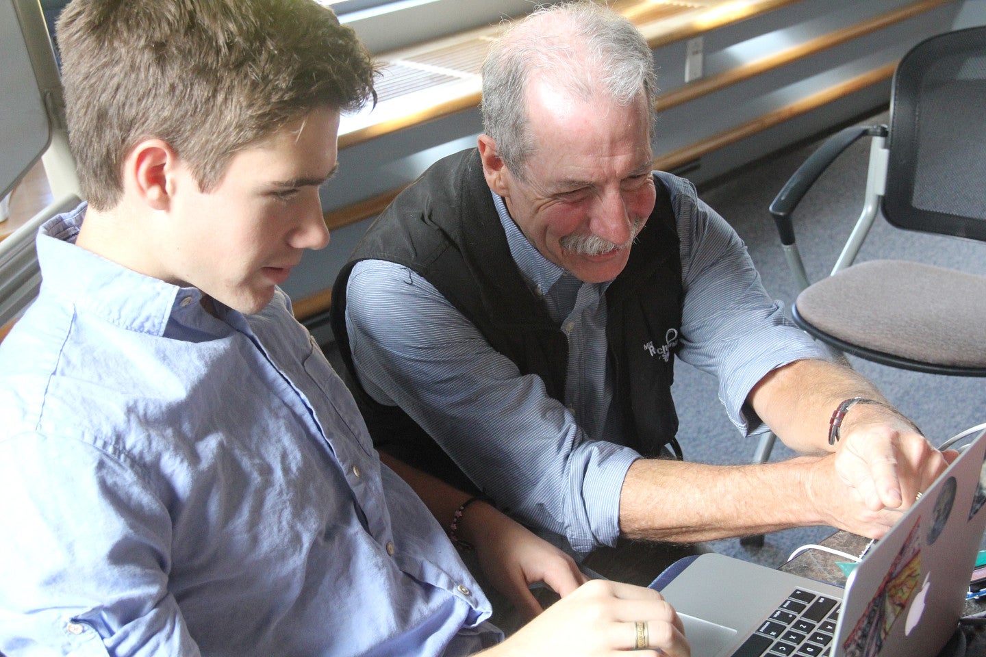 A professor helps a student on a laptop