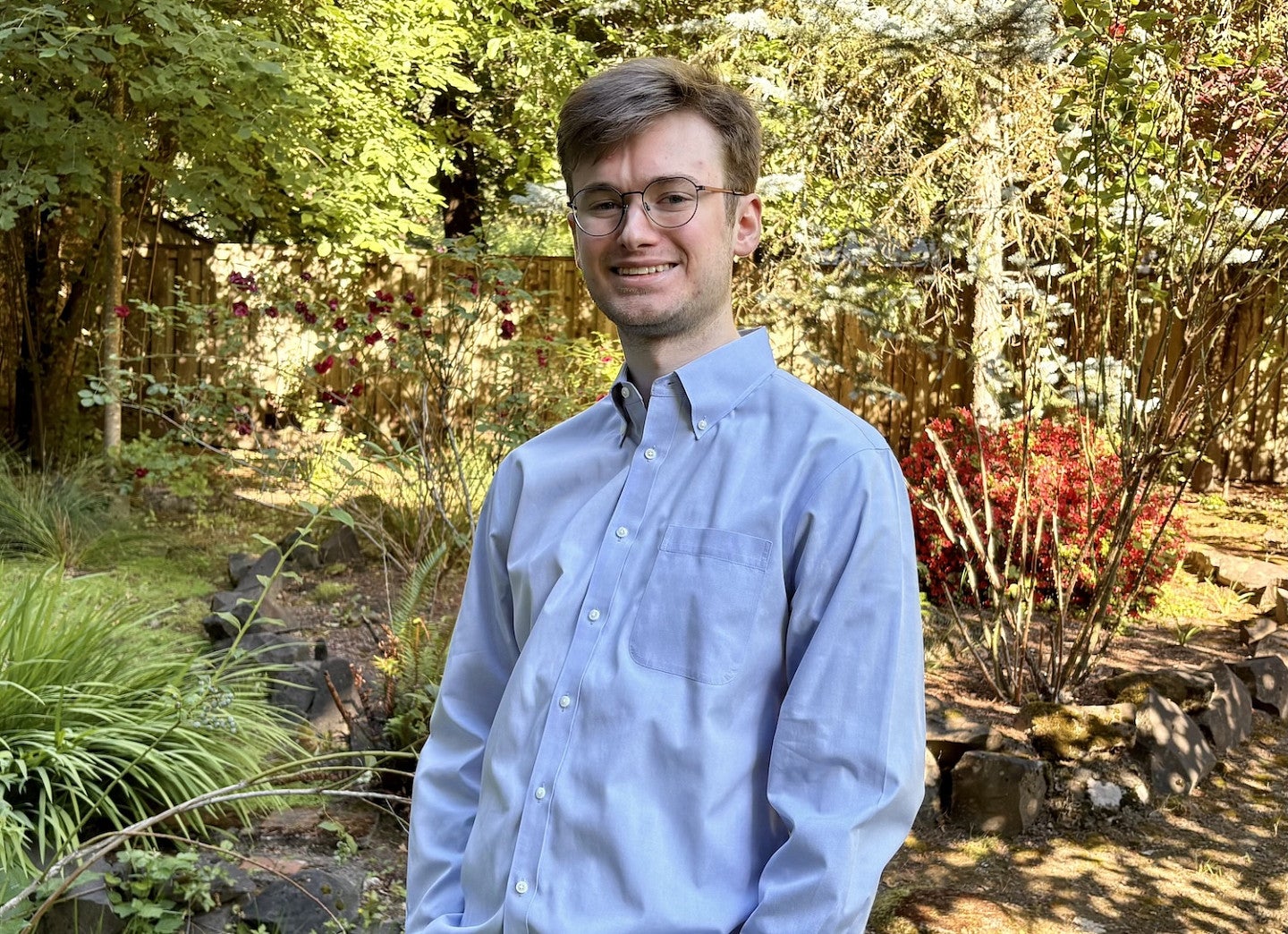 data science alum wearing glasses smiling for photo with greenery in background