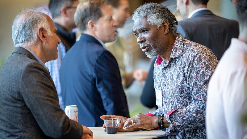 Two men talking in a room full of people