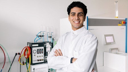 young man in lab coat standing with arms crossed in a lab