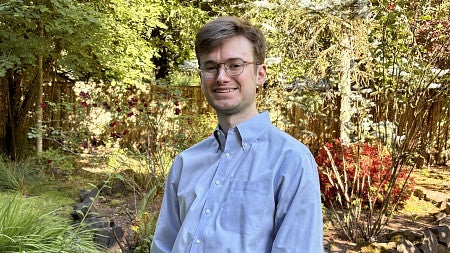 young man wearing glasses smiling for photo with greenery in background