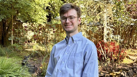 data science alum wearing glasses smiling for photo with greenery in background