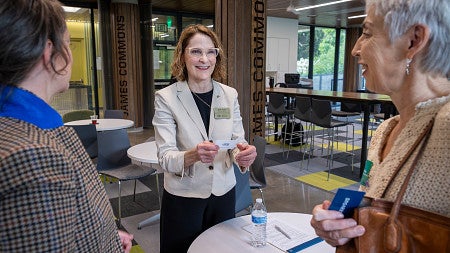 SCDS executive director Beth Plale wearing a cream blazer over a black shirt, smiling and conversing with two individuals at a table.