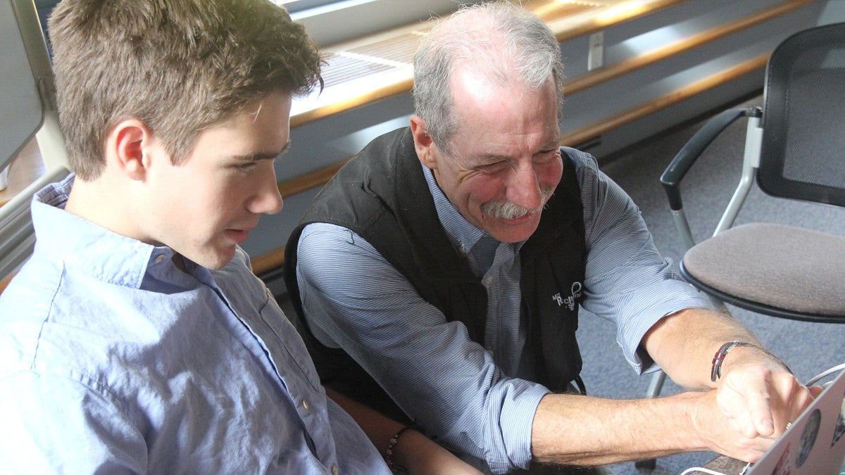A professor helps a student on a laptop