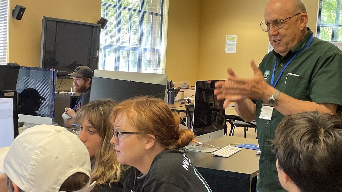 Man speaking to a group of students gathered around a computer