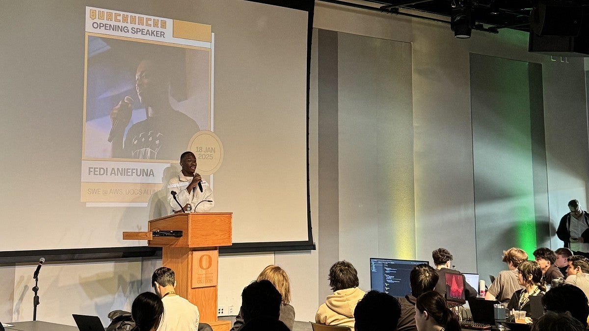 man at podium speaking to room of students during a hackathon
