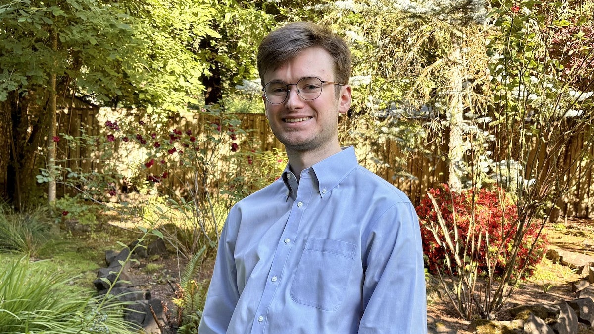 young man wearing glasses smiling for photo with greenery in background