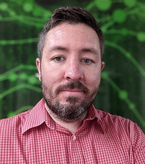 head shot of a man with greenery behind him
