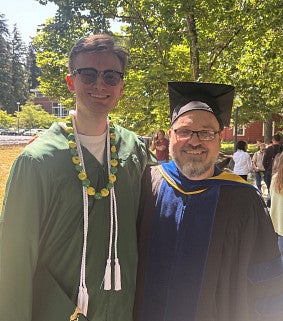 student in graduation regalia posing with professor also in regalia
