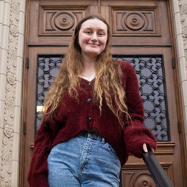 female student posing on steps of chapman hall in front of ornate wooden door