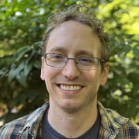 portrait of bespectacled man in front of leafy background