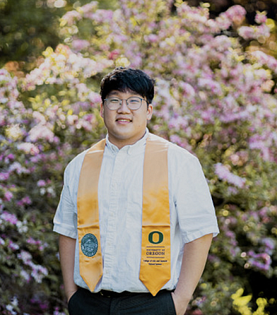 student posing in graduation stole in front of pink flowering bush