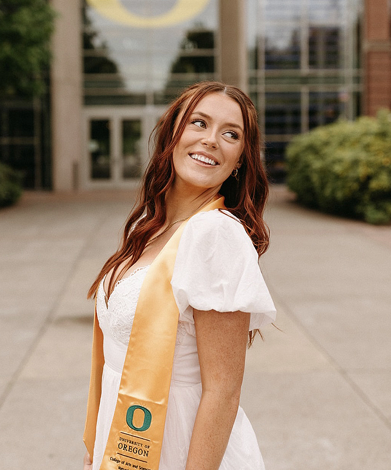 student in graduation stole posing in front of UO campus building Lillis Hall