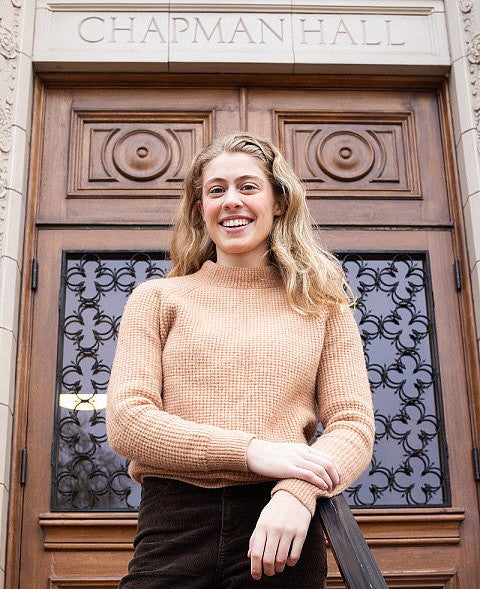 female student posing on steps of chapman hall in front of ornate wooden door
