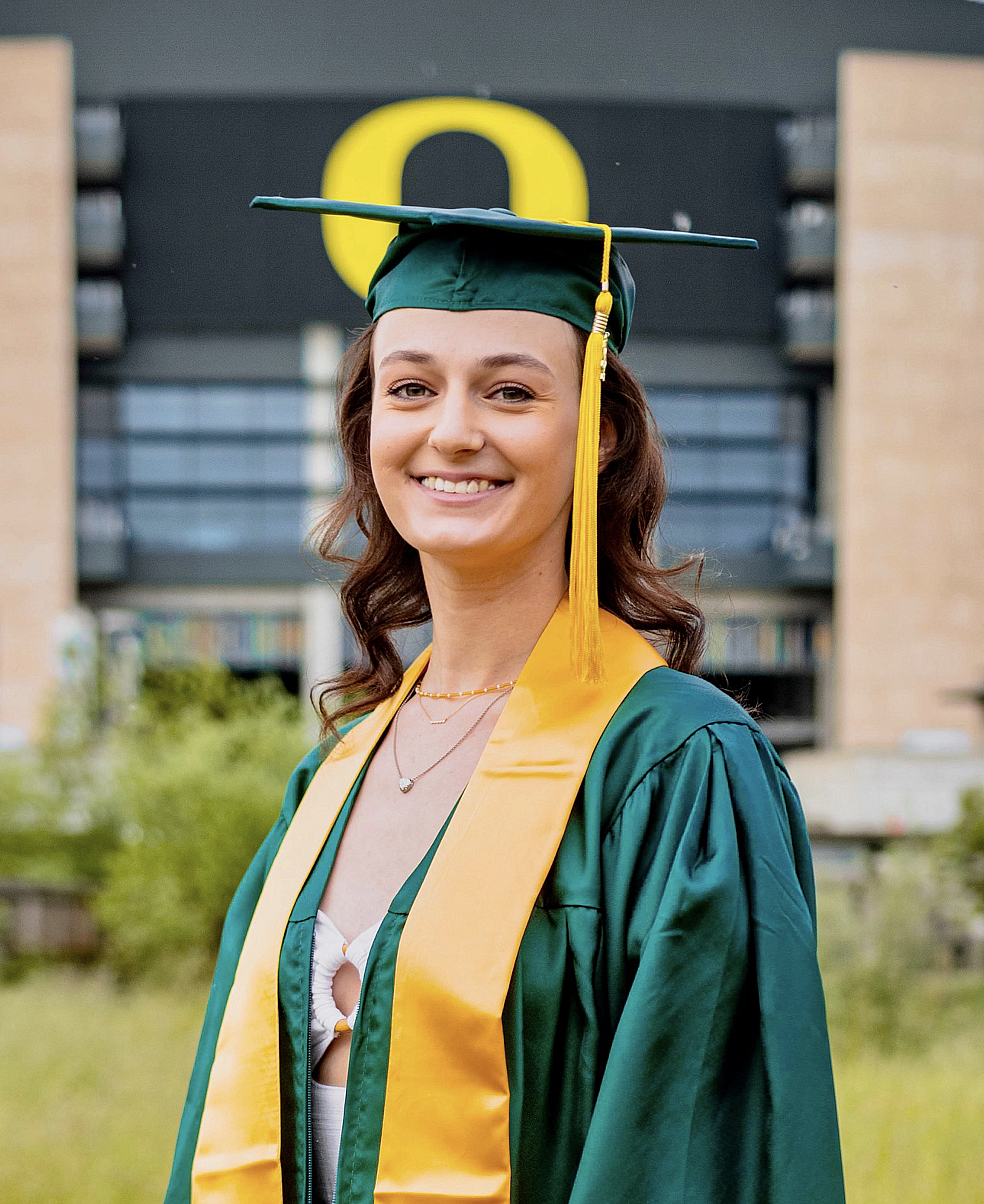 student in graduation cap and gown posing in front of Autzen Stadium