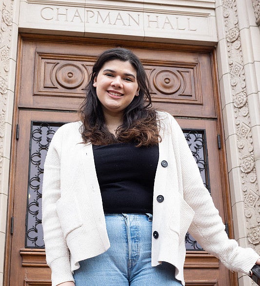 female student posing on steps of chapman hall in front of ornate wooden door