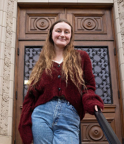 female student posing on steps of chapman hall in front of ornate wooden door