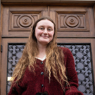 smiling student posing in front of carved wood and wrought iron doors
