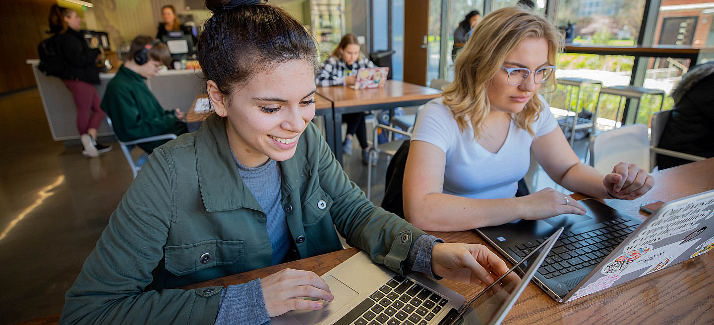 two female students on laptops in a campus cafe