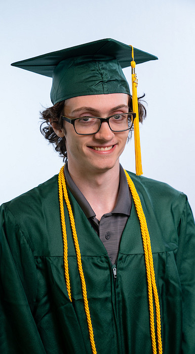 male student in graduation regalia standing in front of white studio background
