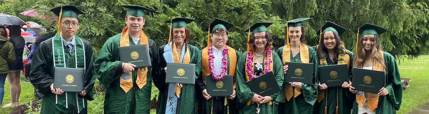 group of students outside in graduation regalia posing with diploma covers
