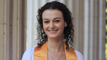 portrait of female student in graduation stole posing in front of white columns