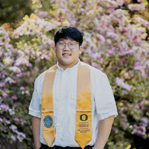 student posing in graduation stole in front of pink flowering bush