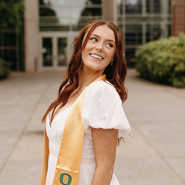student in graduation stole posing in front of UO campus building Lillis Hall