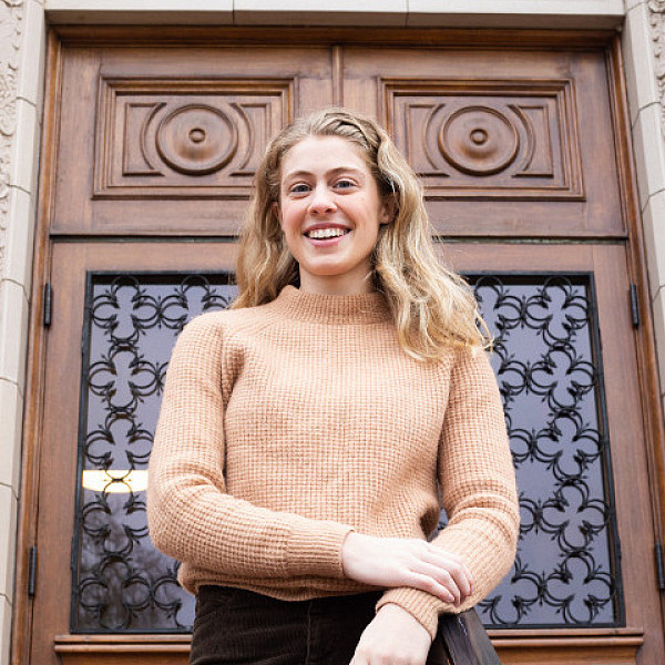 female student posing on steps of chapman hall in front of ornate wooden door