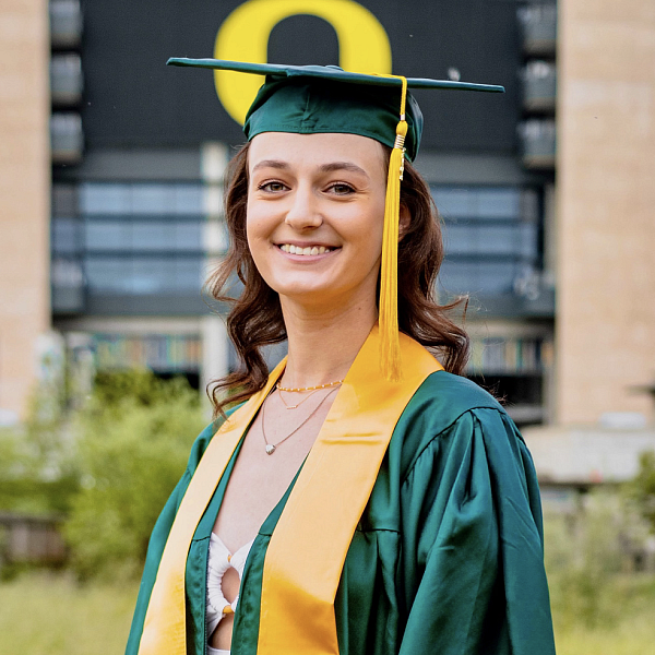 student in graduation cap and gown posing in front of Autzen Stadium
